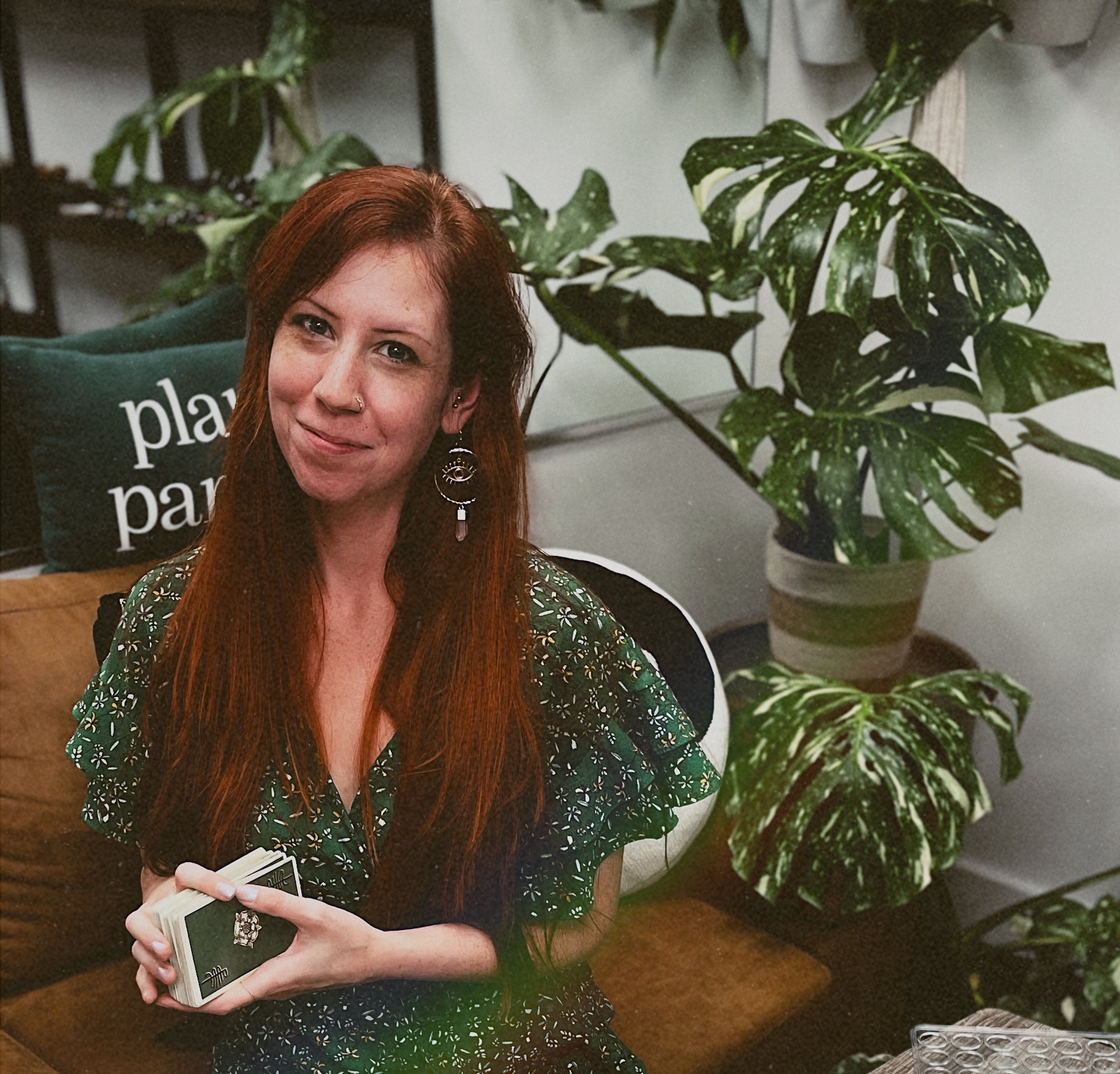 Woman in a green dress sitting on a couch with tarot cards in a cozy indoor setting.